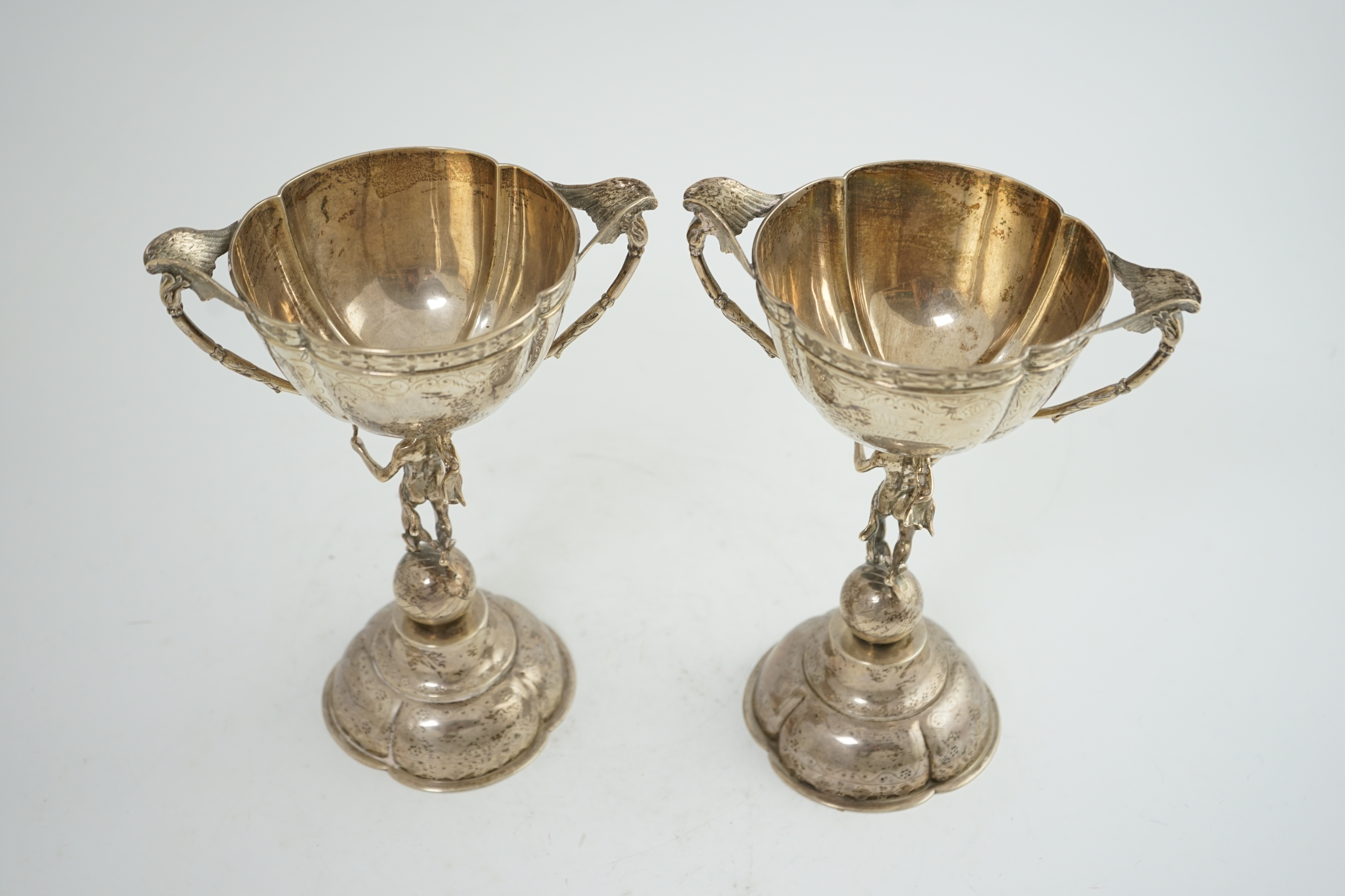 A pair of Victorian silver two handled pedestal cups, each figural stem modelled as Hermes upon a globe, by Edward Charles Brown